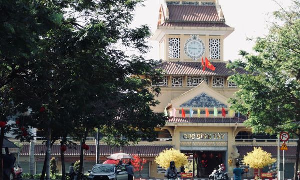 Scenic view of the iconic Binh Tay Market entrance with surrounding trees and vibrant flags in Ho Chi Minh City, Vietnam.