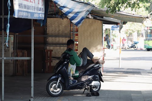 A Man Sitting on a Motor Scooter Parked on the Sidewalk in City 