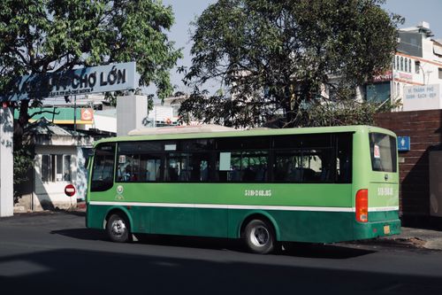 Free Green public bus parked on a street in Ho Chi Minh City, Vietnam, under a tree on a sunny day. Stock Photo