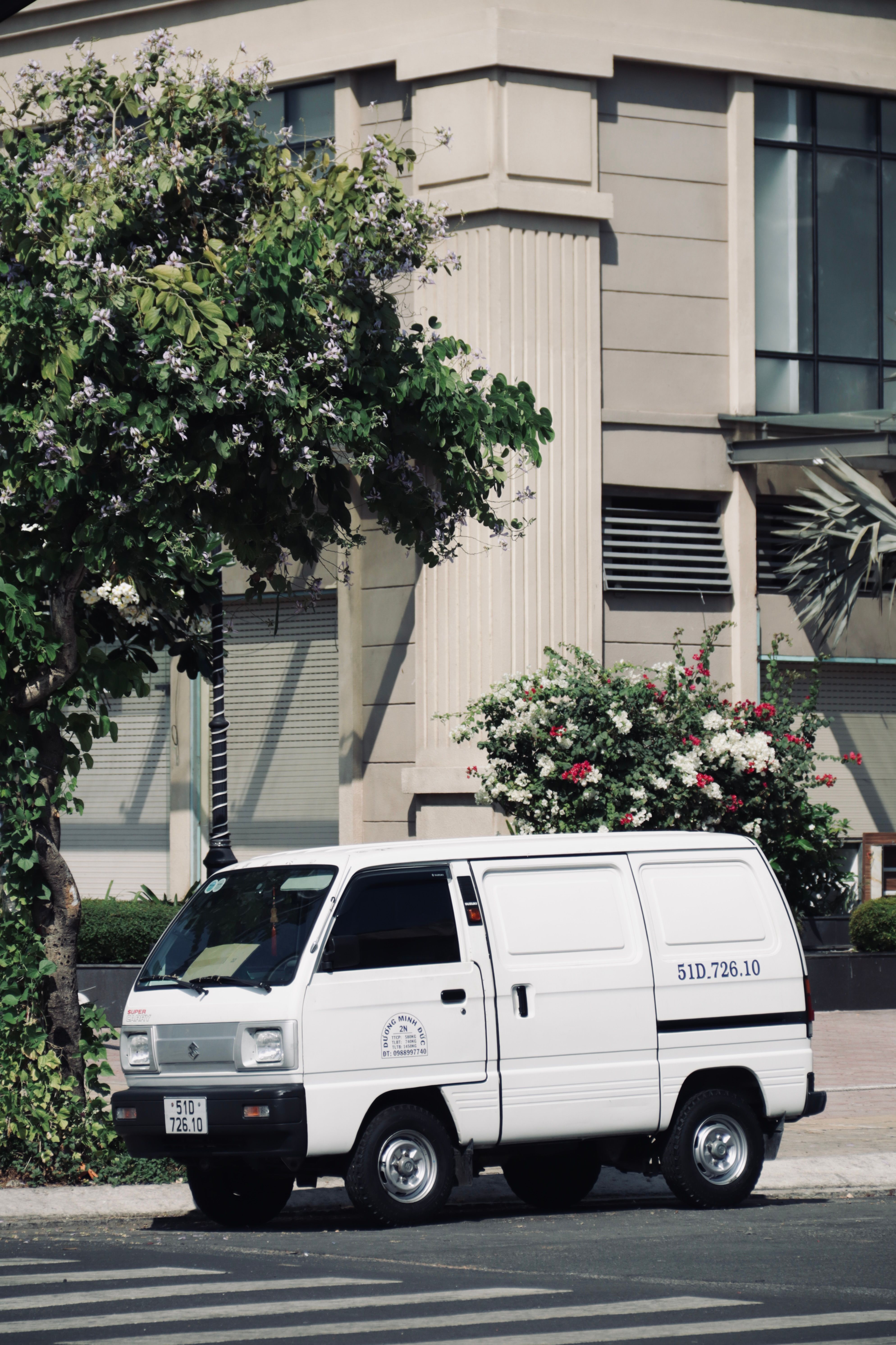 A white van parked on a city street surrounded by greenery and urban architecture.