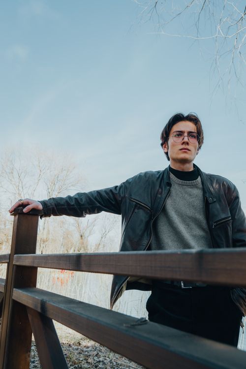 Free Man in black leather jacket standing by wooden fence, exuding a stylish look. Stock Photo