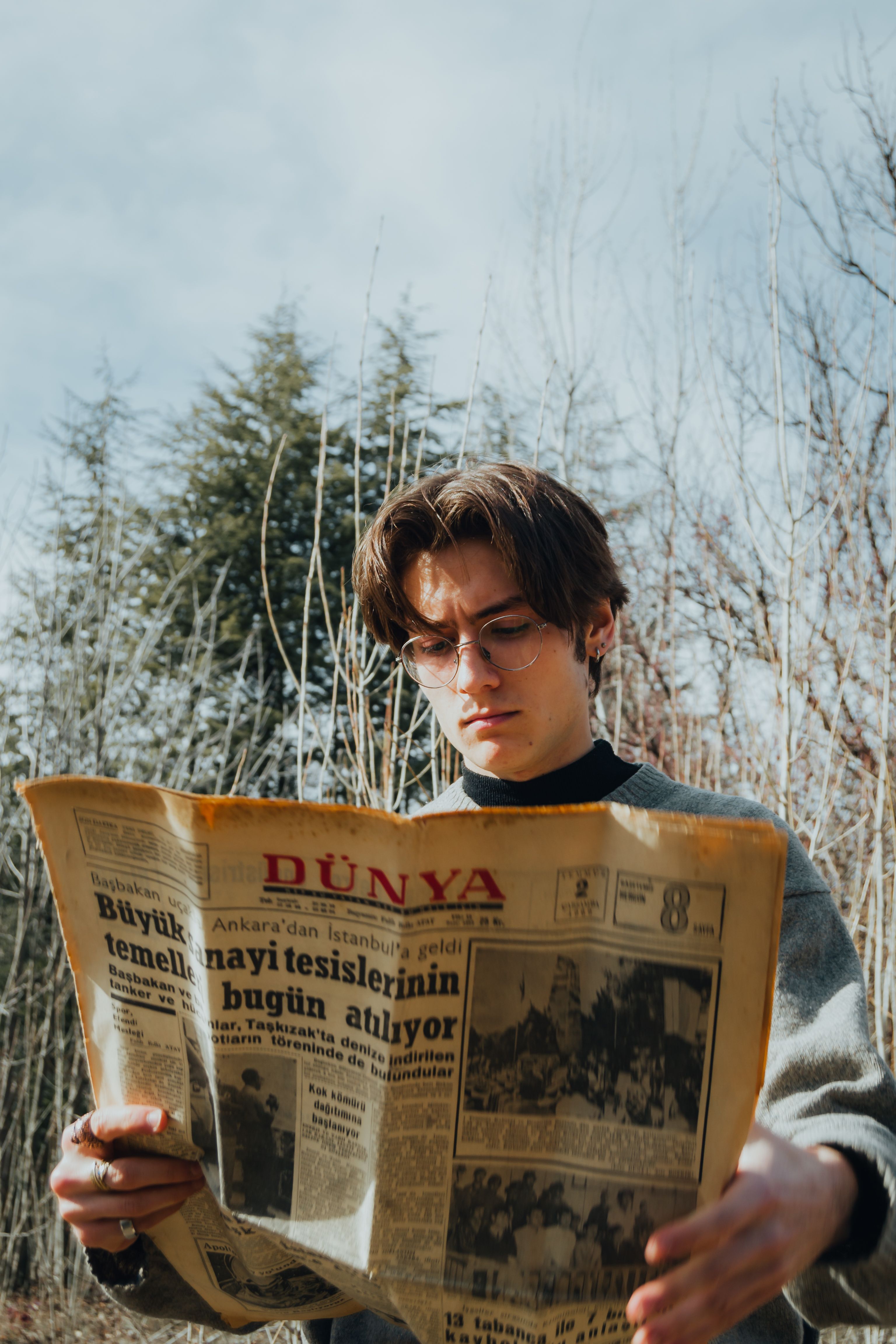 A young man with sunglasses reads an old newspaper outdoors on a sunny day.