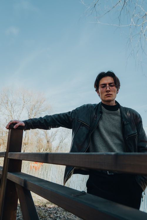 Free Fashionable man in a leather jacket standing by a wooden fence on a clear day. Stock Photo