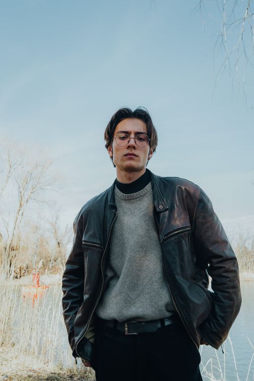 Free Portrait of a man in a leather jacket standing outdoors on a clear day, hands in pockets. Stock Photo