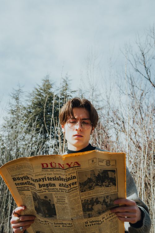 Free A young man with glasses reads a newspaper outdoors in a winter setting. Stock Photo