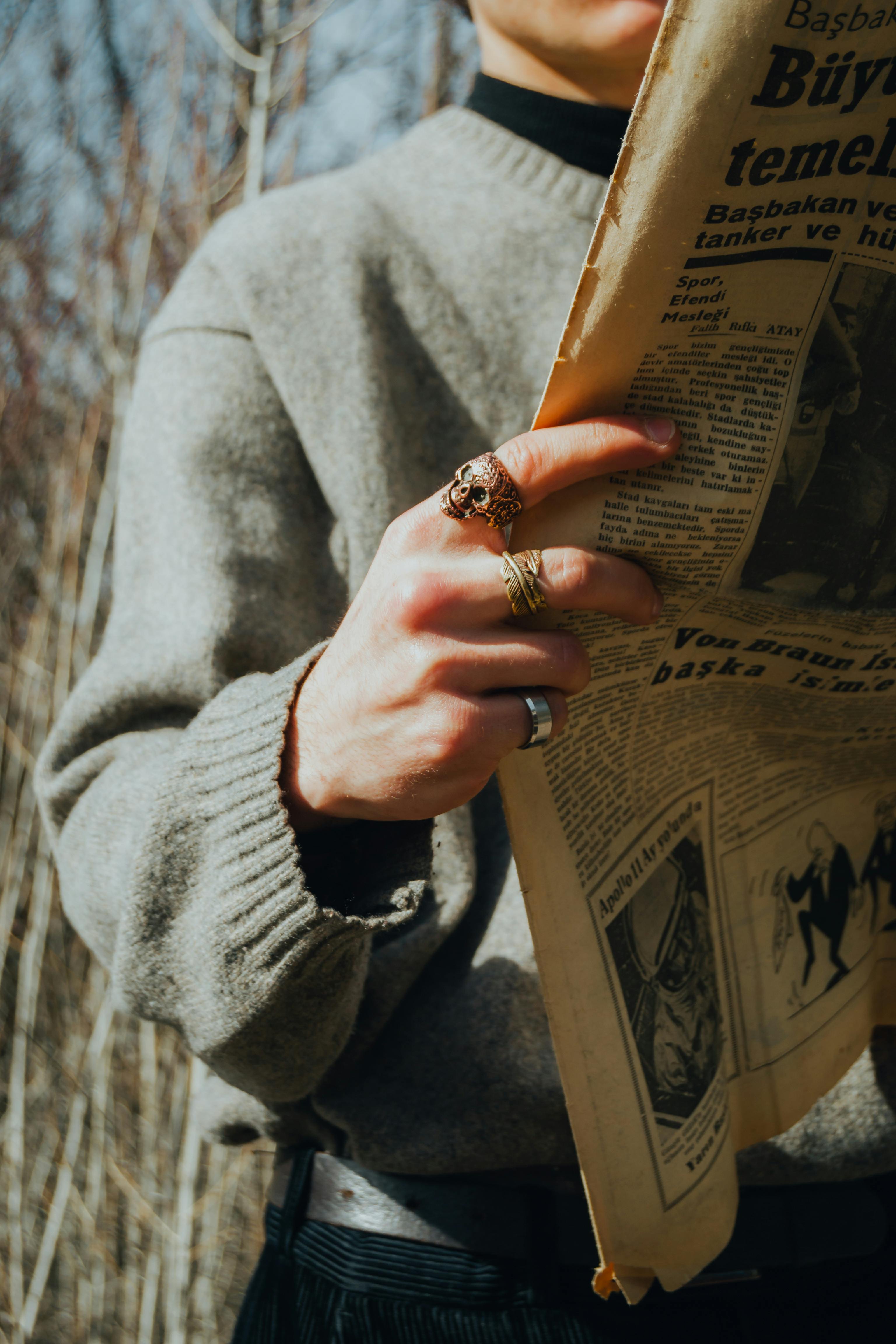 close up of a man in a sweater holding a newspaper while standing outside