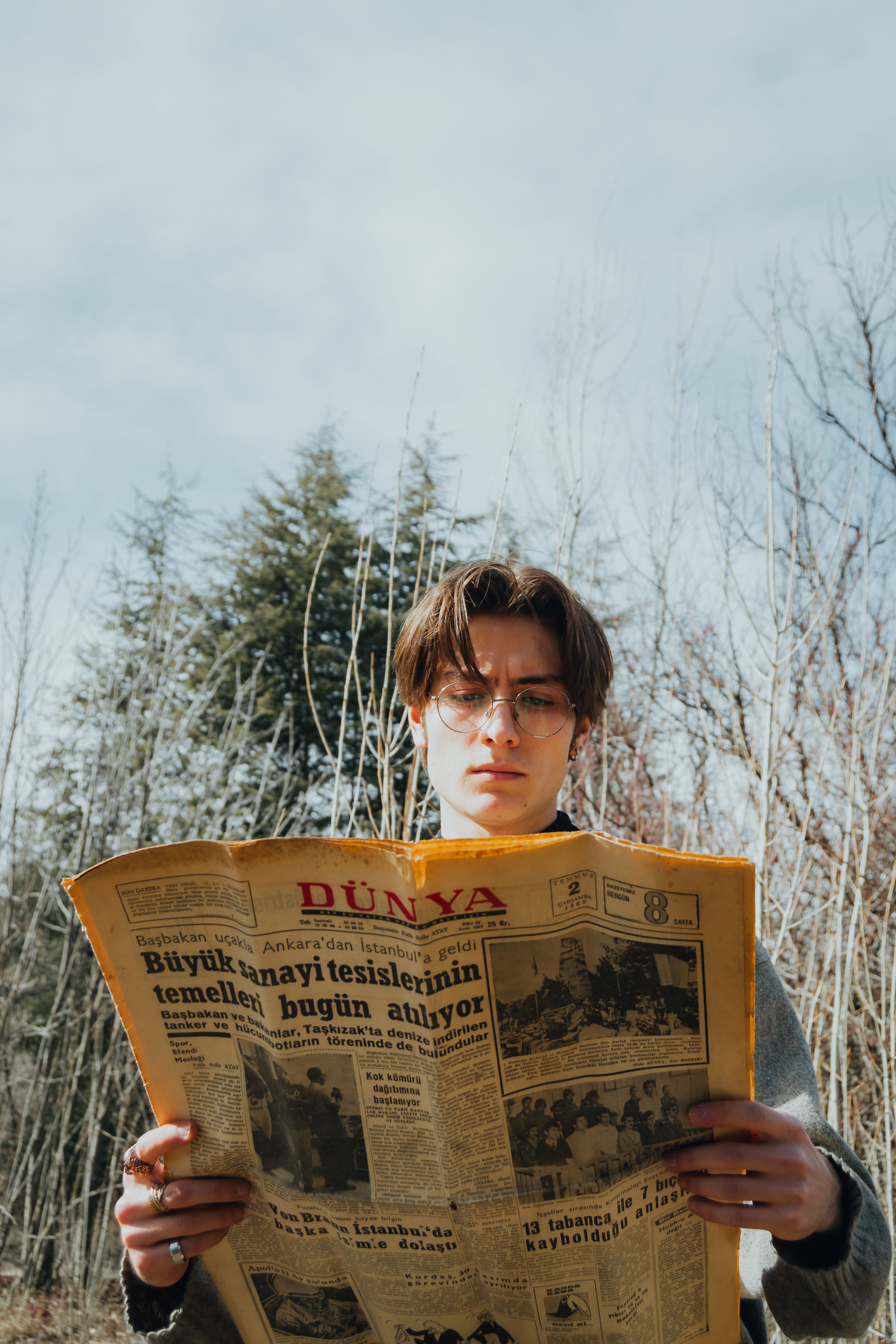 Caucasian man with eyeglasses reading a newspaper outdoors in the fall forest.