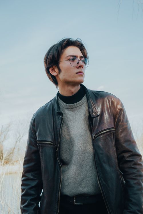 Free Portrait of a young man wearing glasses and a leather jacket outdoors. Stock Photo