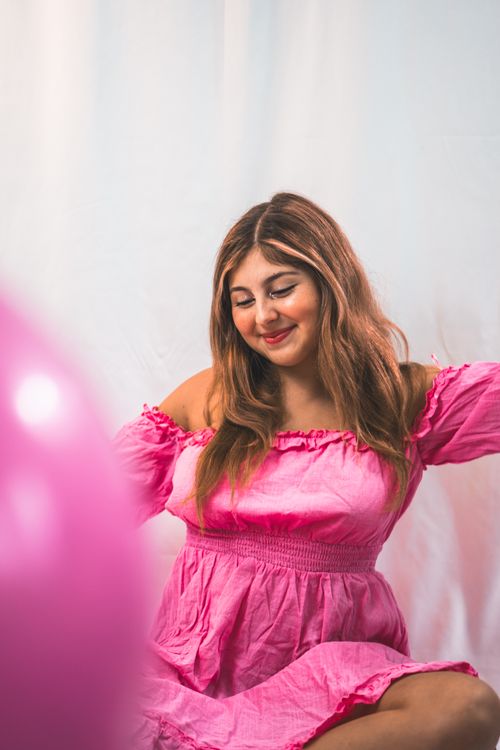 Free Elegant portrait of a woman smiling in a bright pink dress against a white studio background. Stock Photo
