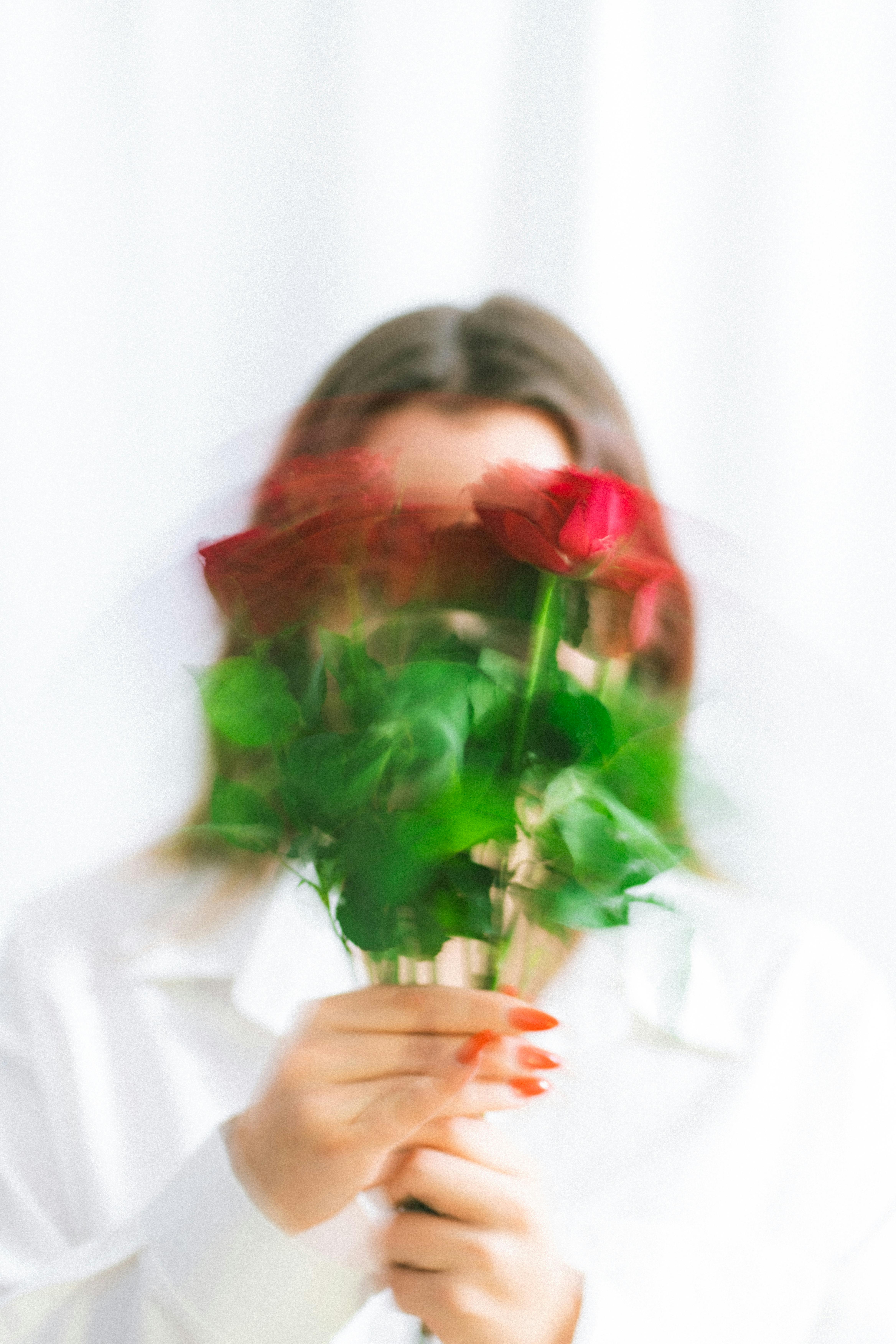 Artistic portrait of a woman holding a blurred bouquet of red roses against a white background.