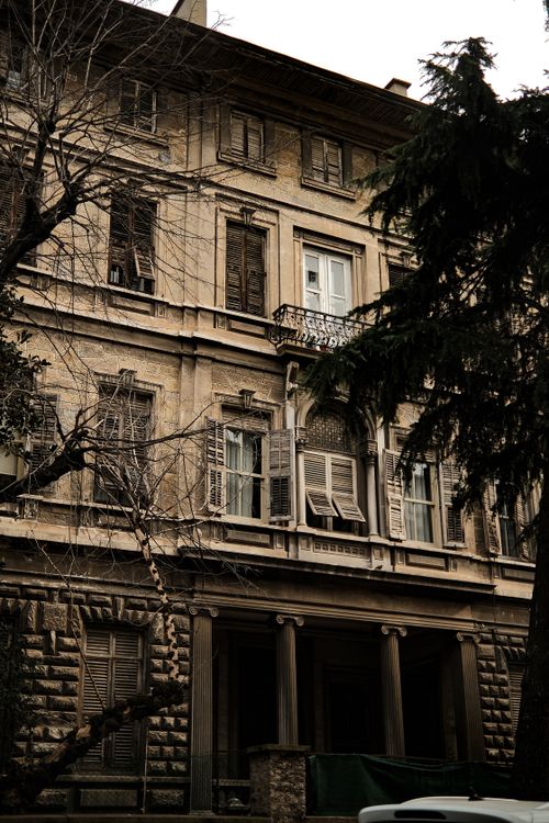 Free A classic old residential building exterior with distressed shutters and tall trees. Stock Photo