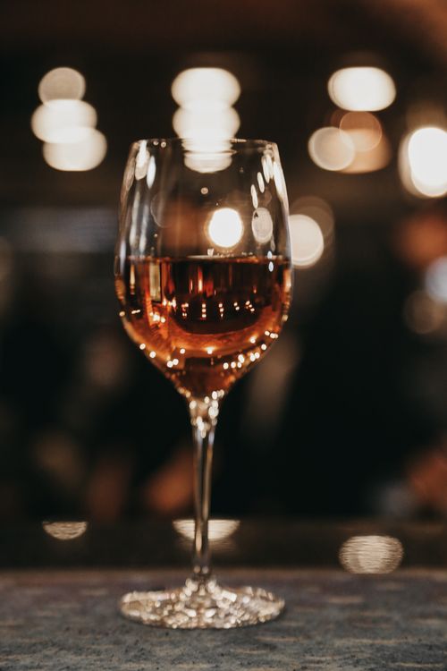 Free A stylish wine glass filled with rose wine against a blurred background with bokeh lights. Stock Photo