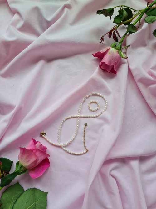 Free Pearl necklace artistically placed on pink silk with fresh pink roses, embodying elegance and romance. Stock Photo