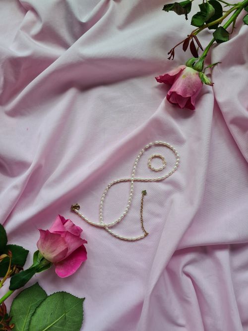 Free An elegant pearl necklace displayed with blooming roses on soft pink fabric. Stock Photo