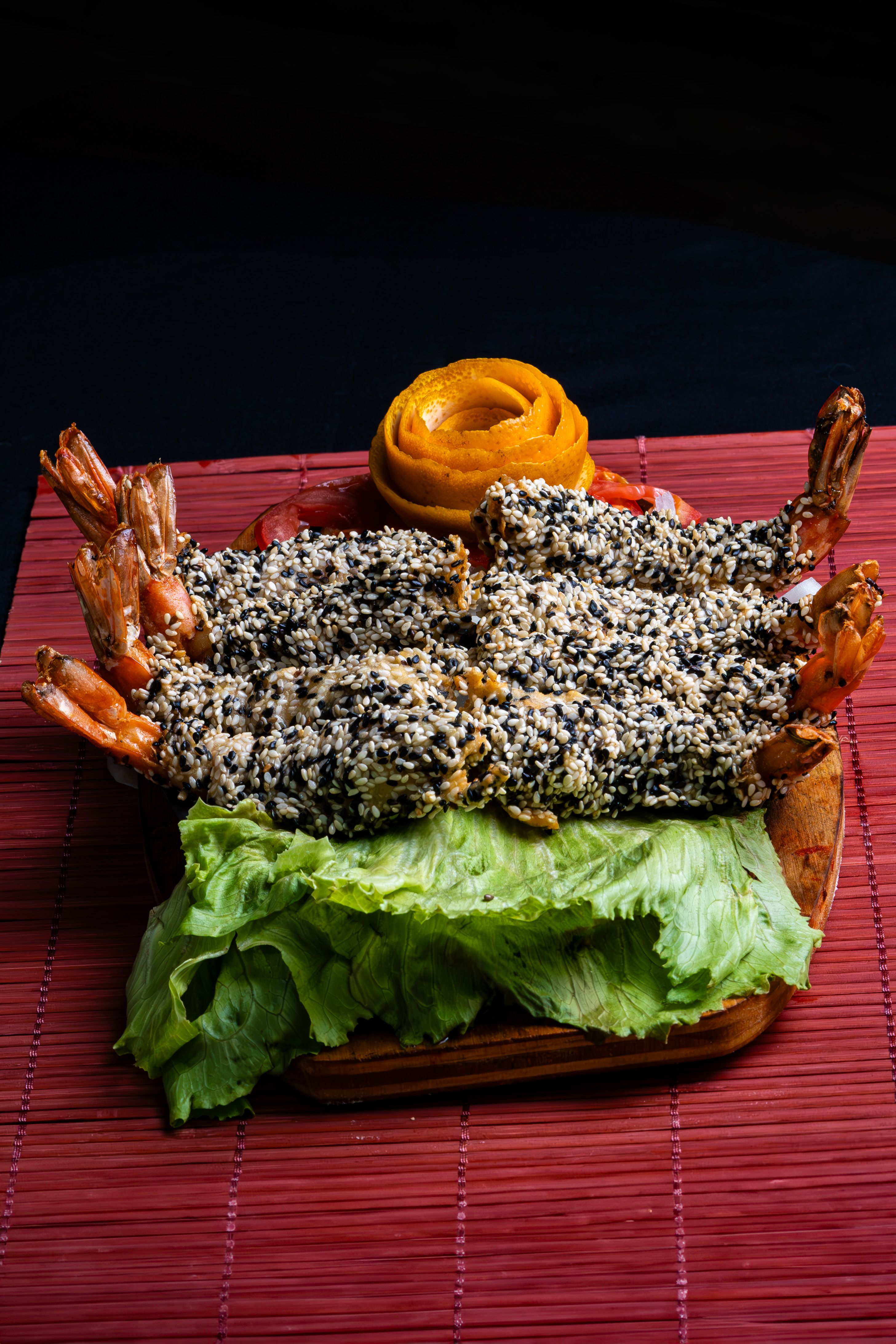 Close-up of crispy sesame-coated shrimp on lettuce, beautifully garnished with a carved fruit rose.