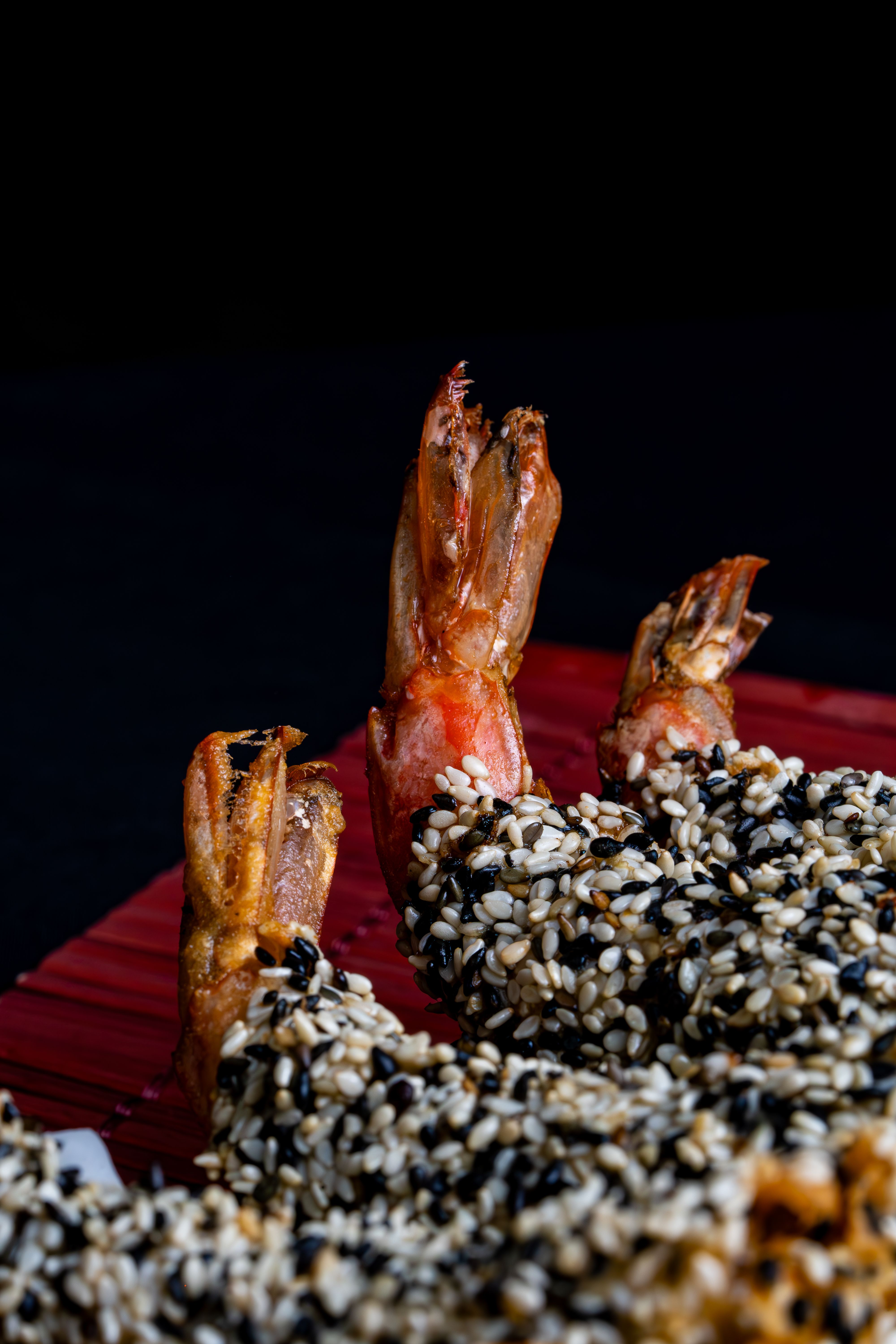 A detailed close-up of crunchy sesame seed crusted shrimp on a dark backdrop.