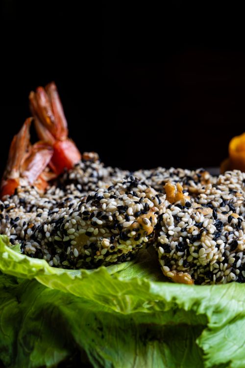 Free Close-up of sesame-crusted shrimp on a fresh lettuce bed with a dark background. Stock Photo