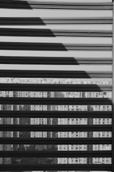 Black and white cityscape seen through blinds, creating an abstract urban feel.