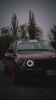 Moody shot of a vintage red car with illuminated headlights outdoors.