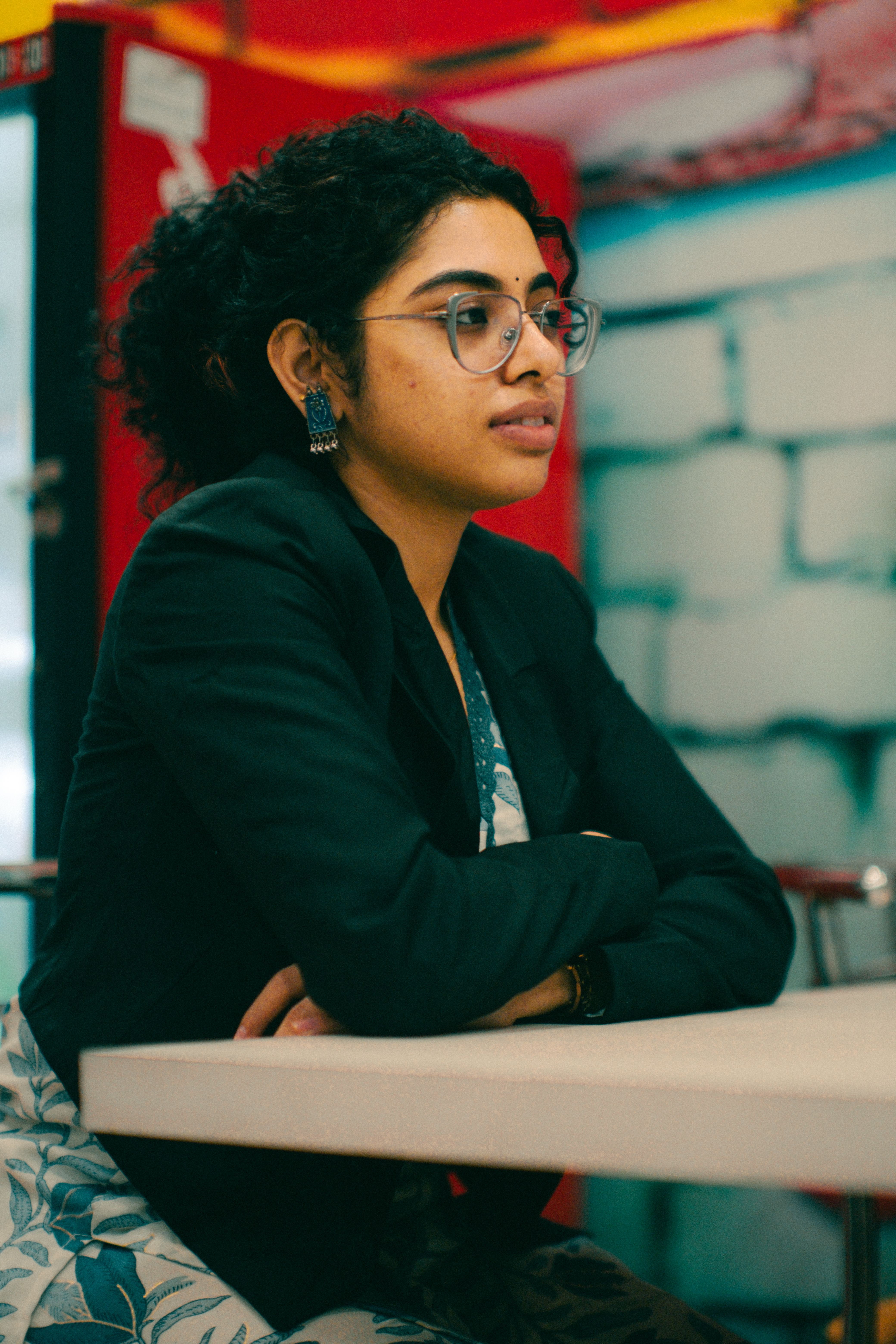 Portrait of a confident woman with glasses sitting indoors at a table.