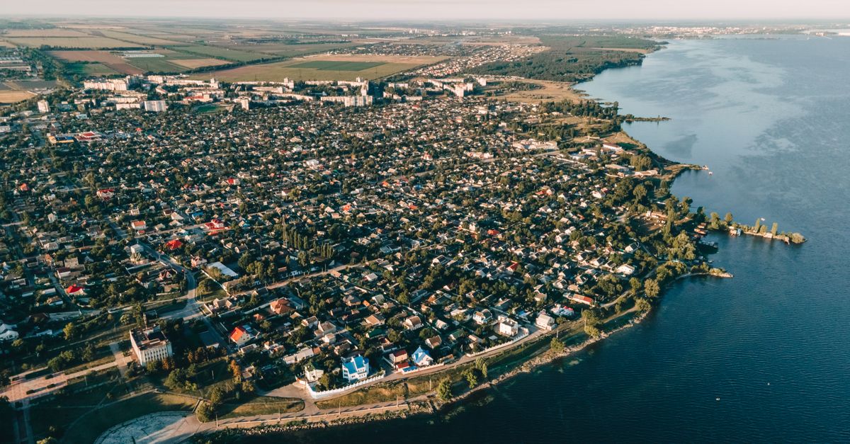 Aerial view of a sprawling coastal city with houses, roads, and waterways under clear skies.