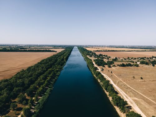 Free Expansive aerial shot of a river flanked by lush trees and sprawling agricultural fields under a clear sky. Stock Photo