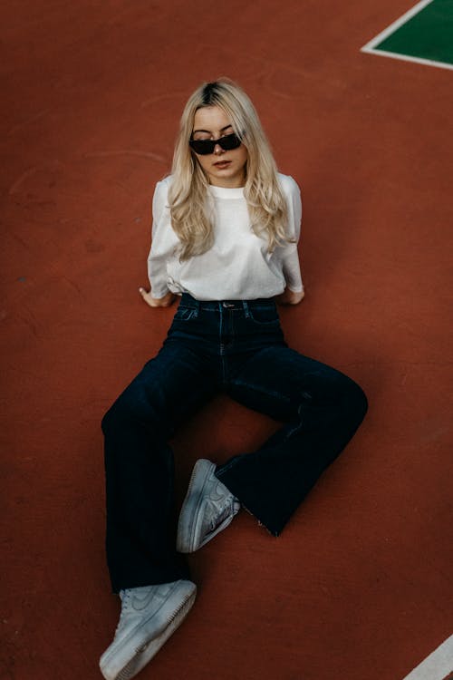 A woman sitting on a tennis court wearing jeans and a white shirt