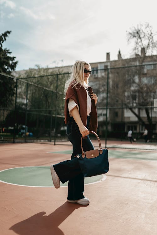 A woman in jeans and a jacket is walking on a basketball court