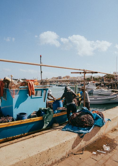 Free Fishermen working on boats in the vibrant Marsašlokas harbor, Malta. Stock Photo
