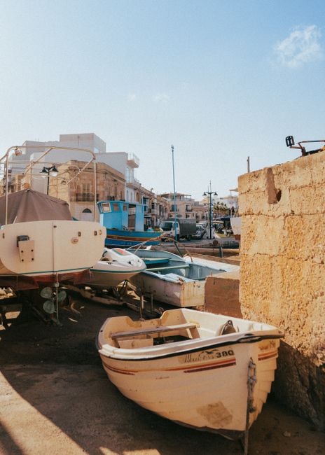 A sunlit boat yard featuring various boats under a clear blue sky in Marsaxlokk, Malta.