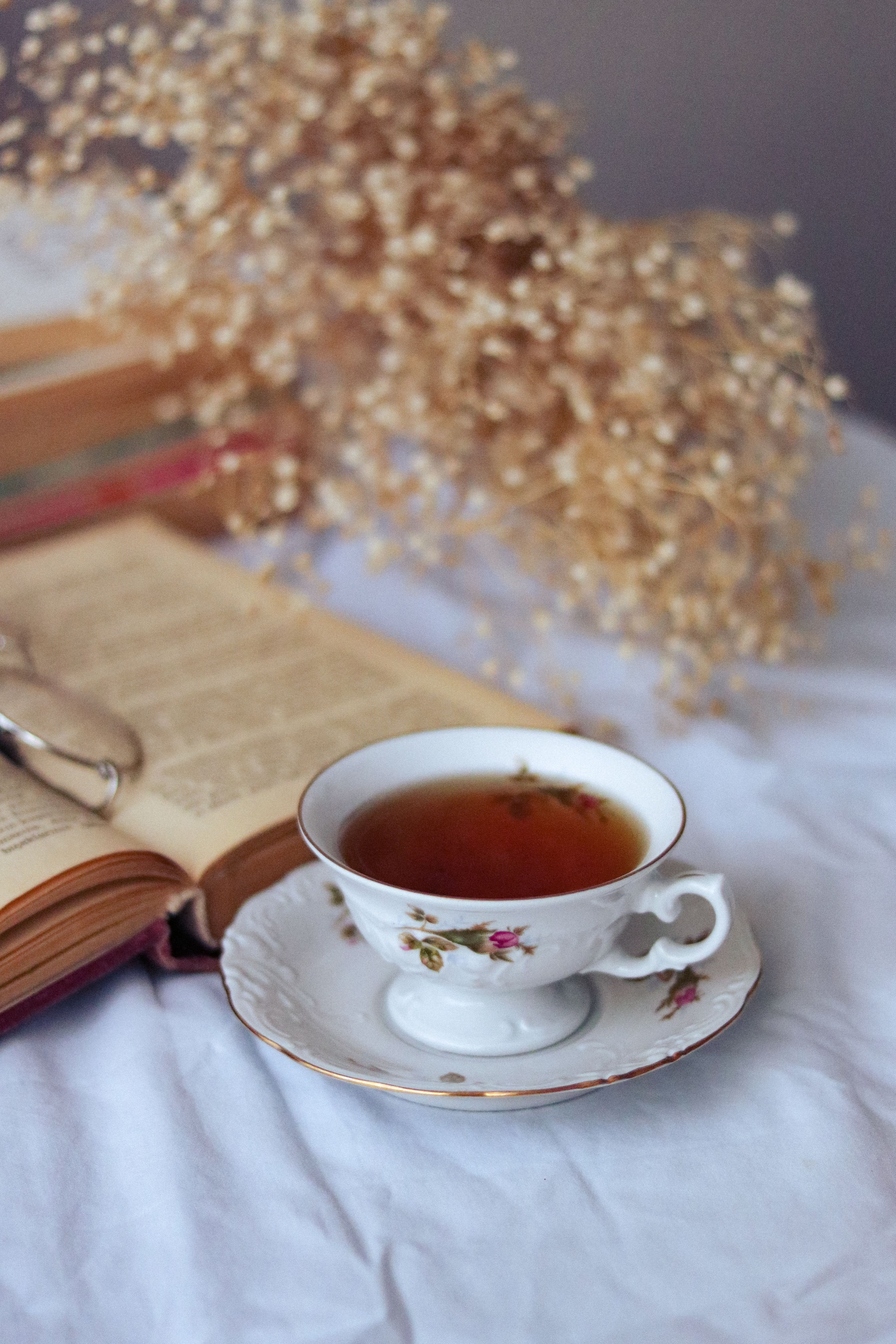 Enjoy a relaxing tea time with an open book and elegant dried flowers in a porcelain cup setting.