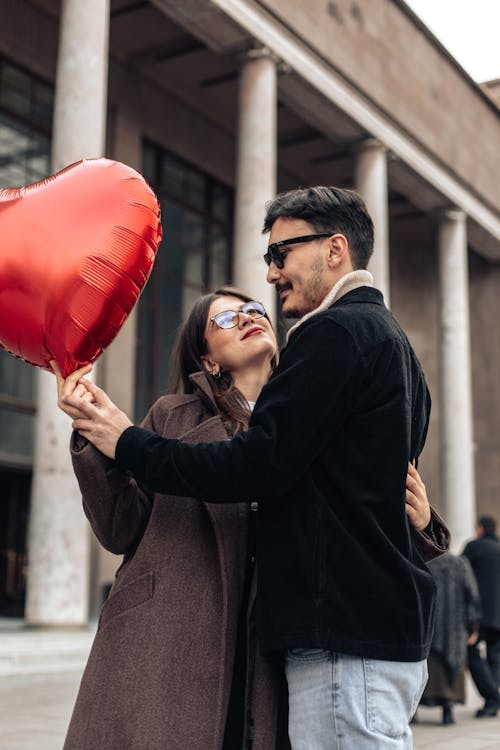 A Couple Holding a Heart Shaped Balloon Standing on a Sidewalk
