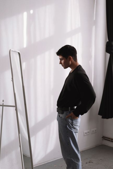 Young man in casual wear observing his reflection in a Berlin room.