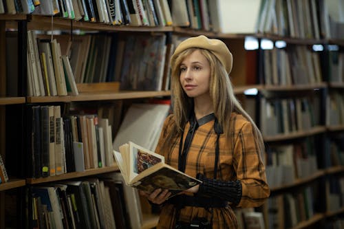 A young woman is standing in a library holding a book