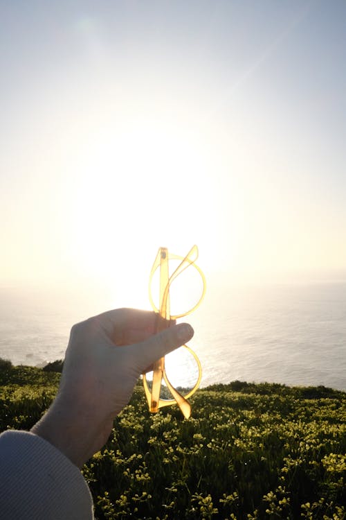 Hand Holding Eyeglasses on Sea Coast at Sunrise