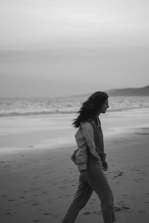 A woman walking on the beach in black and white