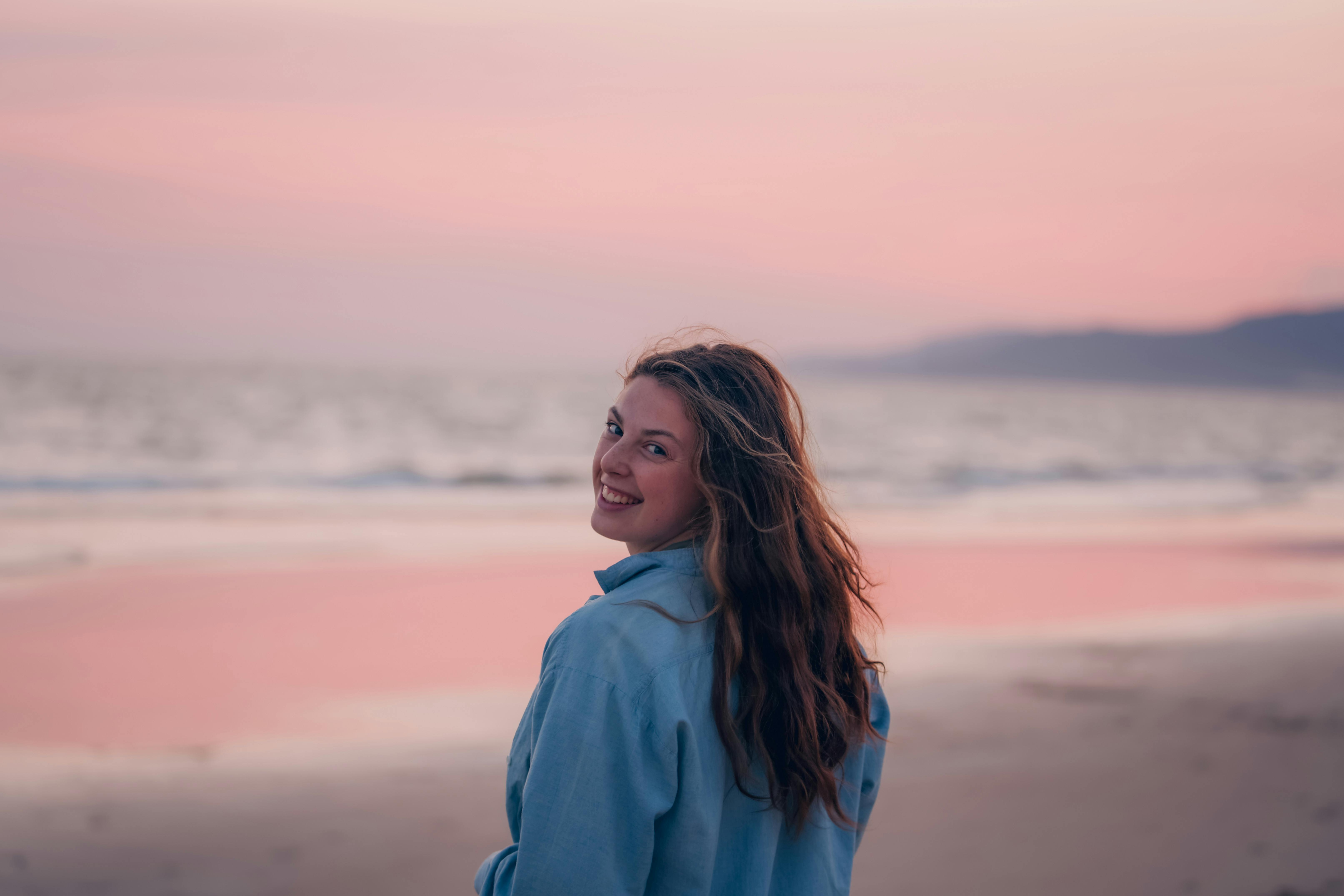 A young woman smiling while enjoying a peaceful sunset on a beautiful beach.