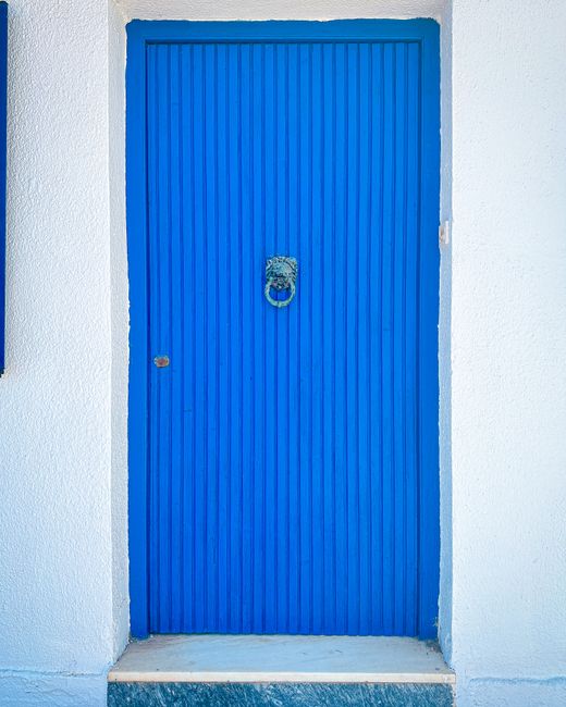 Vibrant blue door on a white wall in Methoni, Greece, showcasing classic Mediterranean architecture.