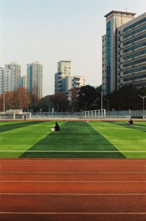 Free View of a Green Stadium with a Running Track and Modern Skyscrapers in the Background  Stock Photo