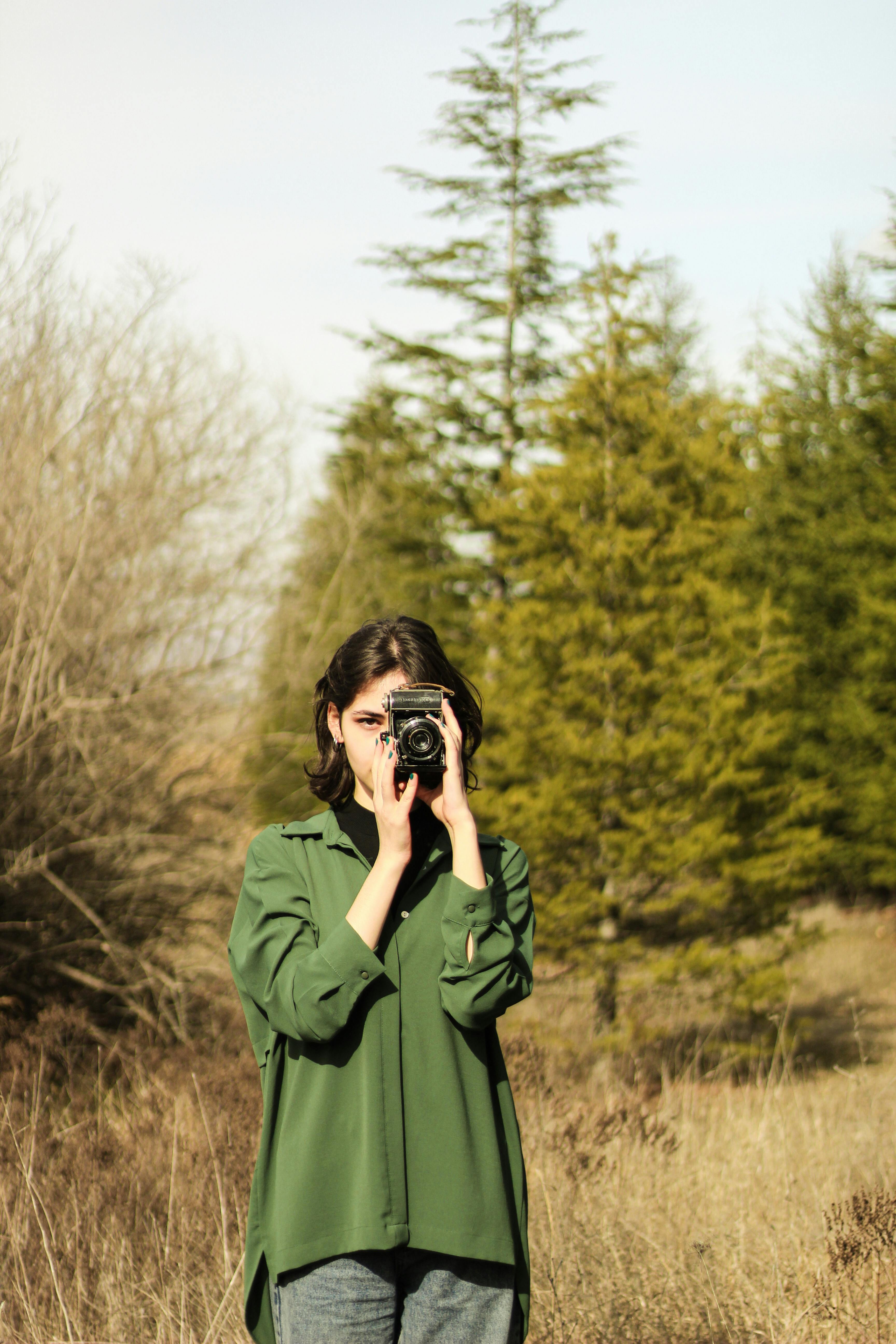Young woman with vintage camera in a sunlit field surrounded by trees.