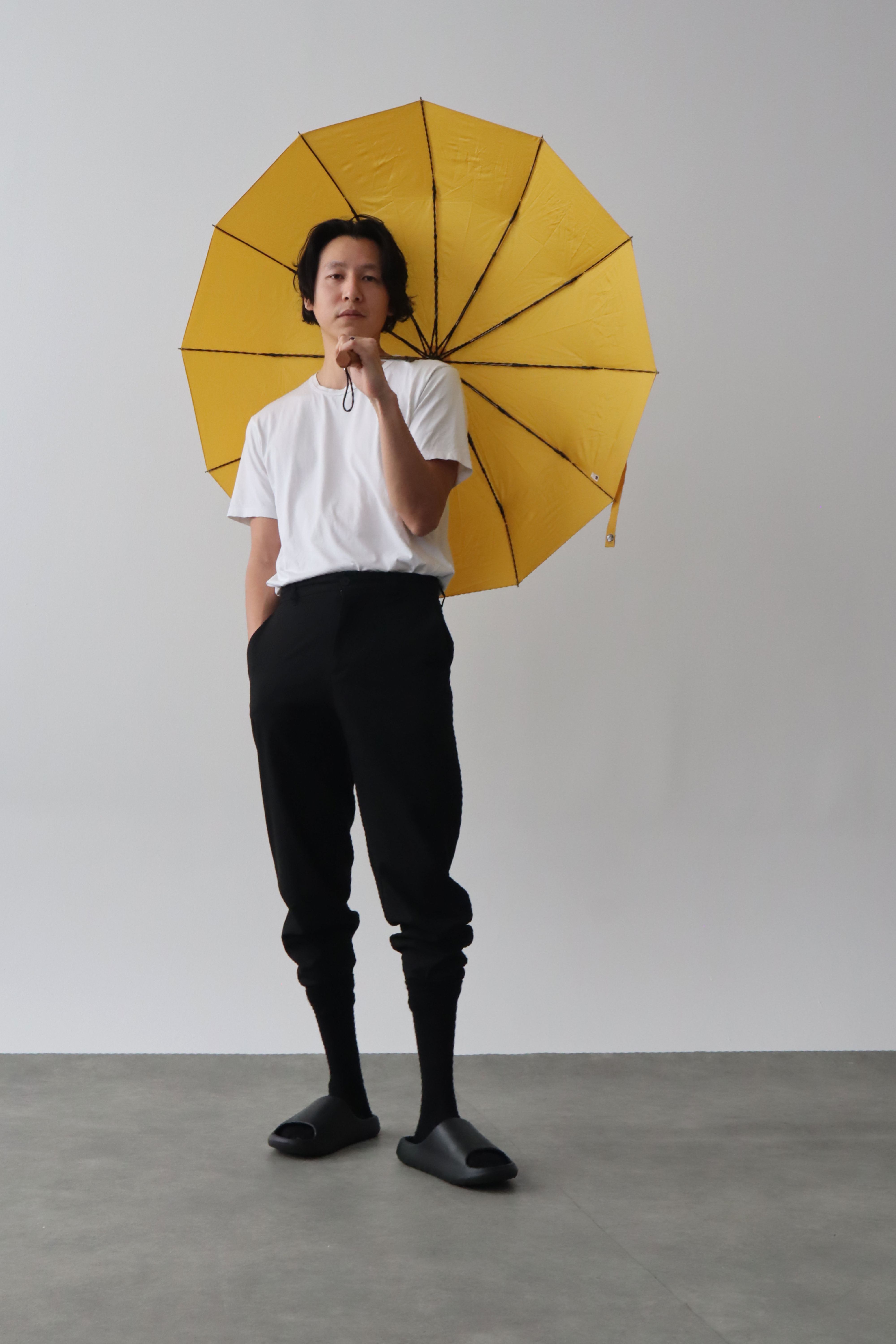 Stylish Asian man in white shirt and black pants holding a yellow umbrella indoors.