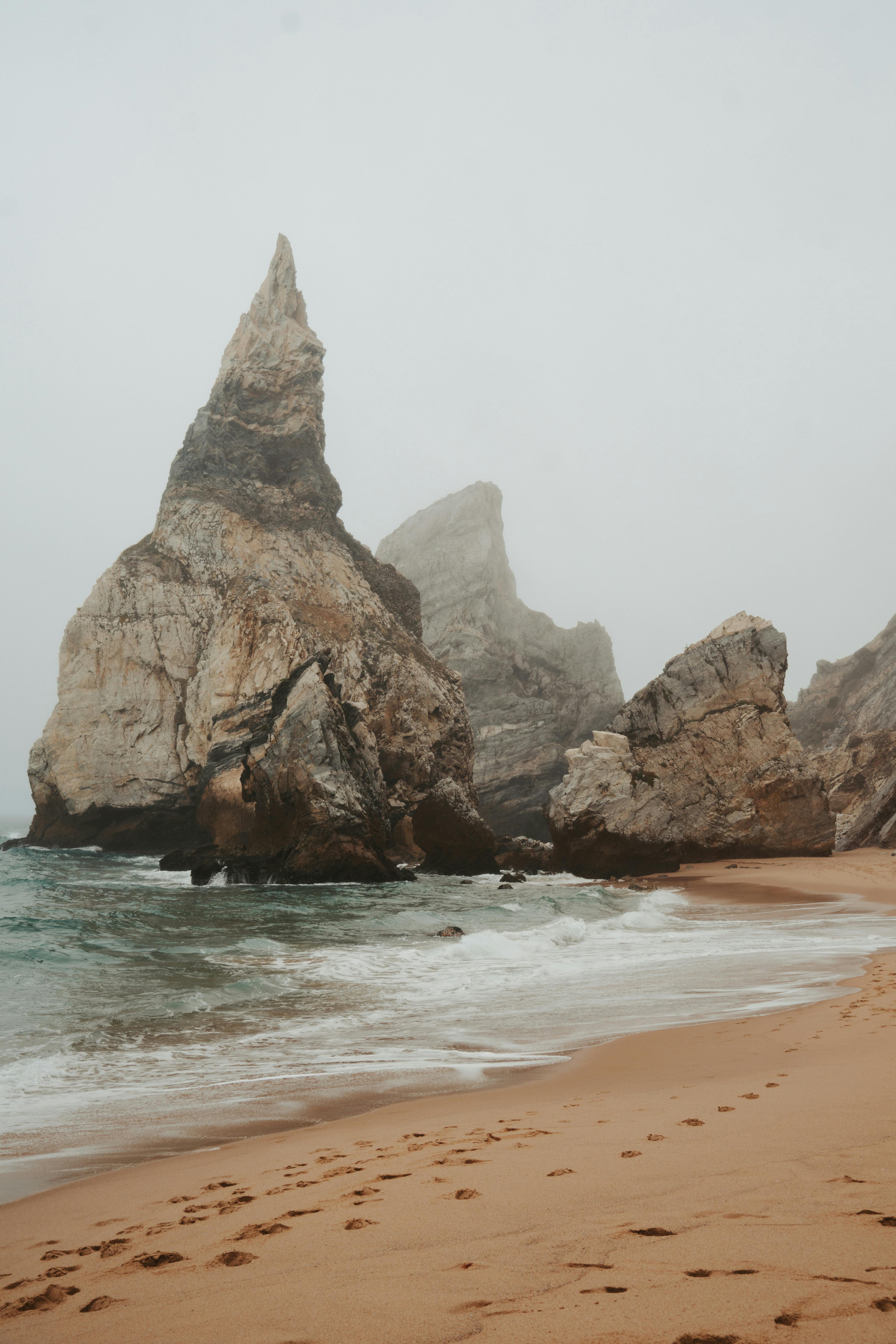 Misty beach scene with towering rock formations and soft waves creating a serene atmosphere.