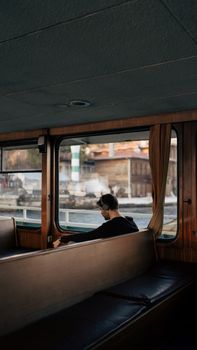 A man wearing headphones relaxes on a ferry with views of İstanbul's cityscape.