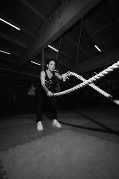 Woman exercising with battle ropes in a gym. Black and white image highlighting dynamic motion.