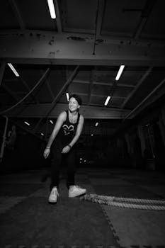 Person smiling in a gym setting, engaging in rope workout, black and white photo.