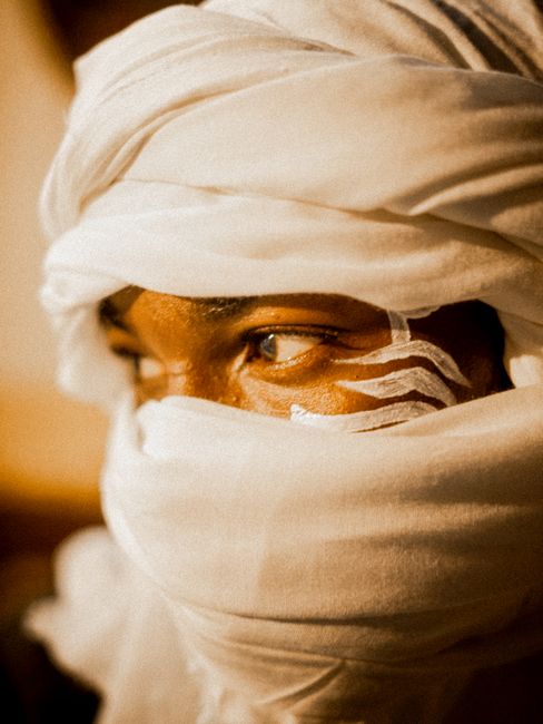 Close-up portrait of a man wearing a white turban with painted designs on his face.