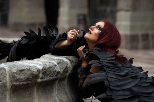 Free Woman with red hair and gothic makeup in a feathery black costume posing dramatically outdoors. Stock Photo