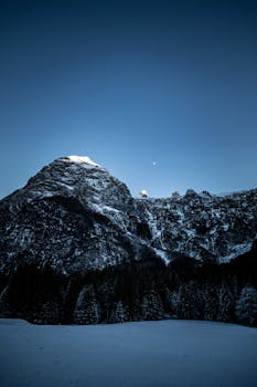 Captivating winter mountain landscape with snow and moon at twilight.