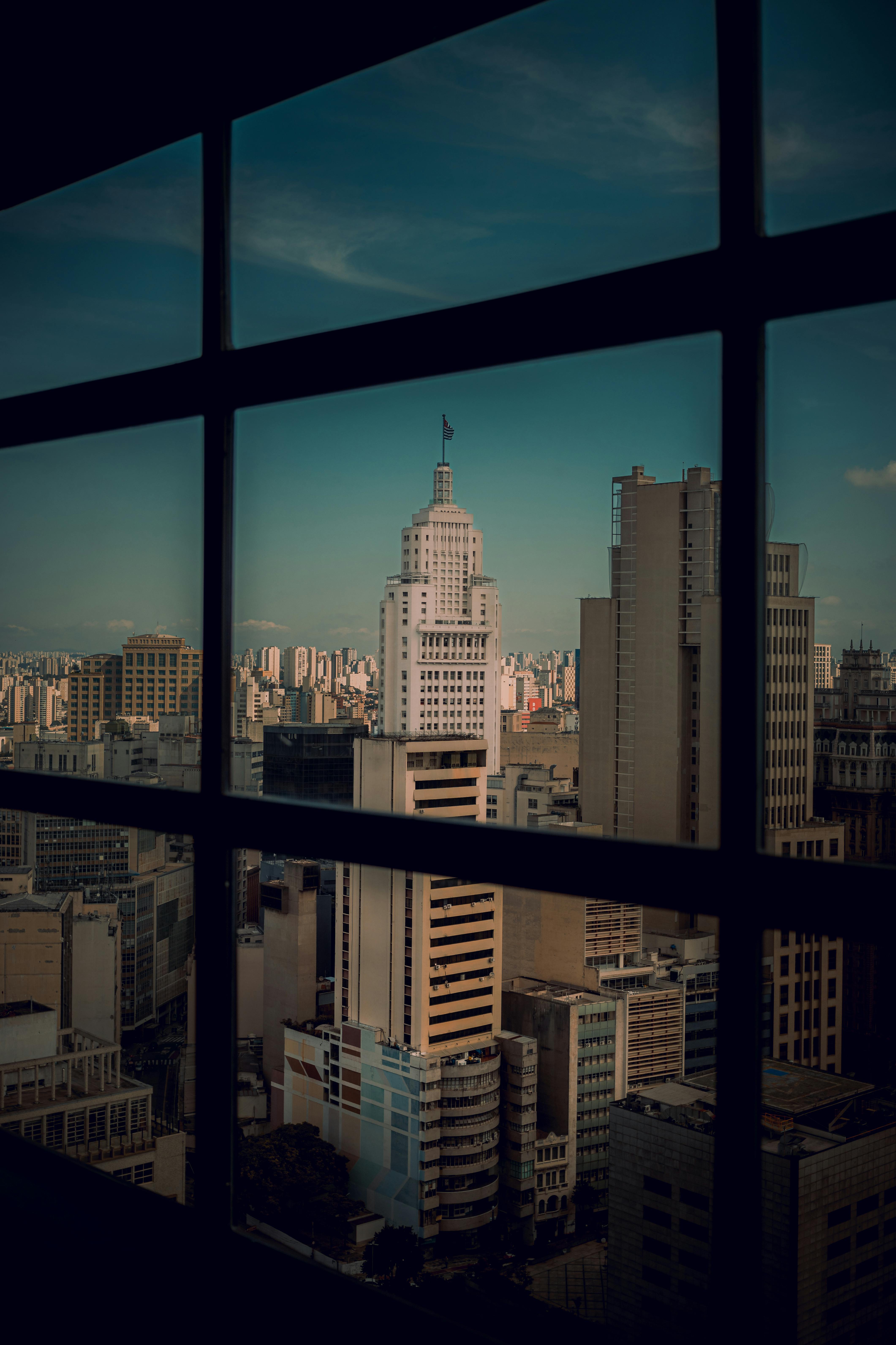 View of Altino Arantes Building amidst São Paulo's skyscrapers, captured through a window frame.