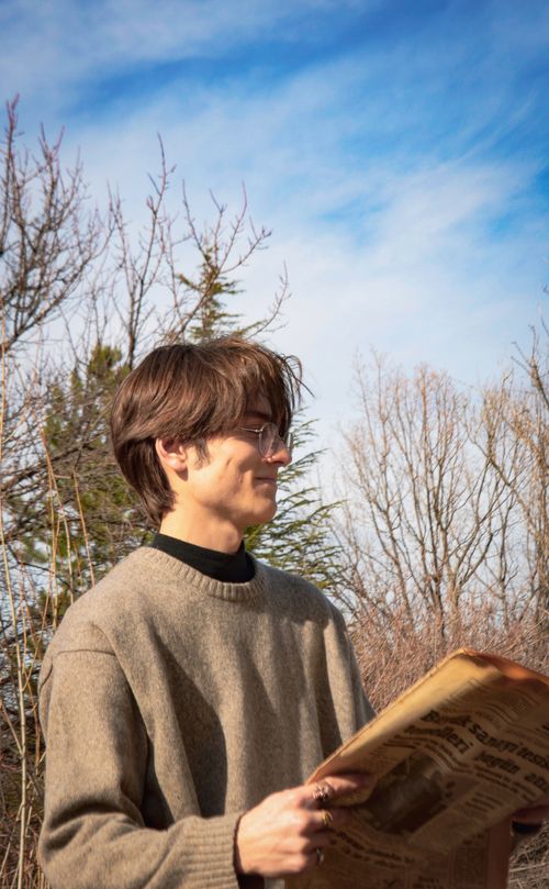 Free Young man in glasses reading a vintage newspaper outdoors on a sunny day. Stock Photo